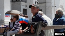 Мужчина с российским флагом сидит перед зданием Мариупольского театра, разрушенным в ходе российской бомбардировки. Мариуполь, 30 мая 2022 года