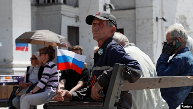 Мужчина с флагом РФ в оккупированном Мариуполе сидит перед разрушенным зданием театра, май 2022 года
