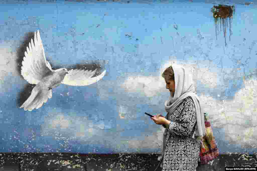 An Iranian woman walks past a mural of a peace dove on a street in downtown Tehran.