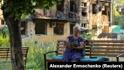Жителька Маріуполя читає книгу на тлі розбитих будинків, 15 липня 2022 року