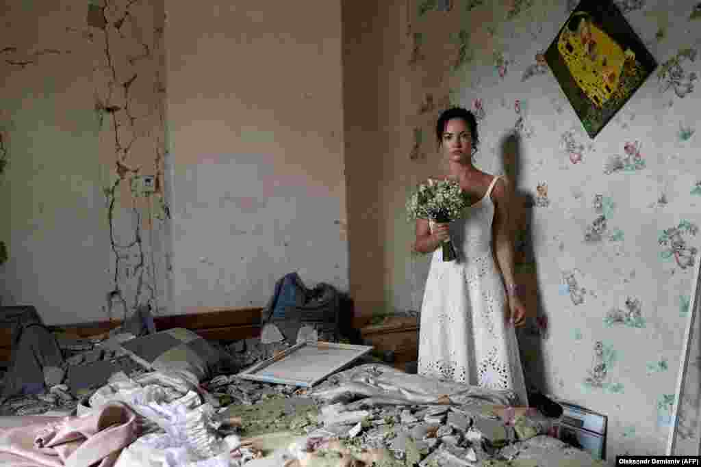 Daria Steniukova, în vârstă de 31 de ani, pozează pentru fotografii de nuntă în apartamentul ei bombardat din Vinița, pe 16 iulie. O rachetă a lovit orașul, aflat la 200 de kilometri sud-vest de Kiev, cu o zi înainte de nunta Steniukovei. Instructorul de yoga a declarat că ea și logodnicul ei erau hotărâți să meargă mai departe cu ceremonia, în ciuda atacului, care a ucis 26 de persoane. &bdquo;Casa mea a fost distrusă, dar nu și viețile noastre&rdquo;, a declarat ea pentru AFP. &bdquo;A fost un mesaj sfidător pentru întreaga lume - subliniind cât de puternici sunt ucrainenii. Suntem pregătiți să ne căsătorim chiar și cu rachete care zboară deasupra capetelor noastre&rdquo;, a mai spus ea. &nbsp;