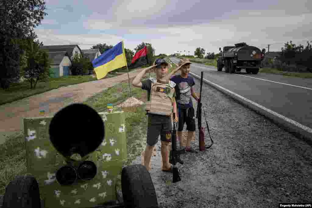 Maksym and Andriy, both aged 11, salute passing Ukrainian soldiers at their &quot;checkpoint&quot; on a highway in the Kharkiv region on July 20.&nbsp;