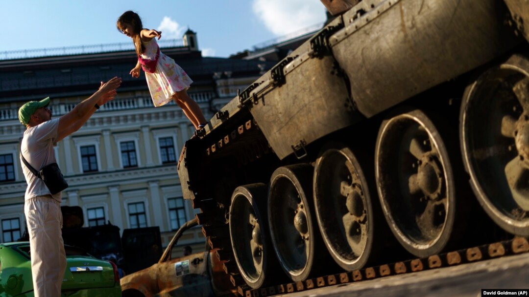 A young girl falls into her father's arms off a destroyed Russian tank on display in Kyiv.
