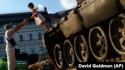 A young girl falls into her father's arms off a destroyed Russian tank on display in Kyiv.