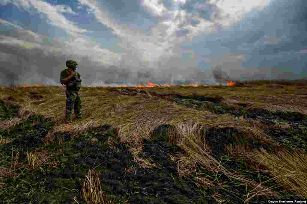 A Ukrainian serviceman stands on a burning wheat field near the front line on the border between the Zaporizhzhya and Donetsk regions.