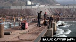 Китайский инженер наблюдает за рабочими, строящими мост через реку в Пакистане.