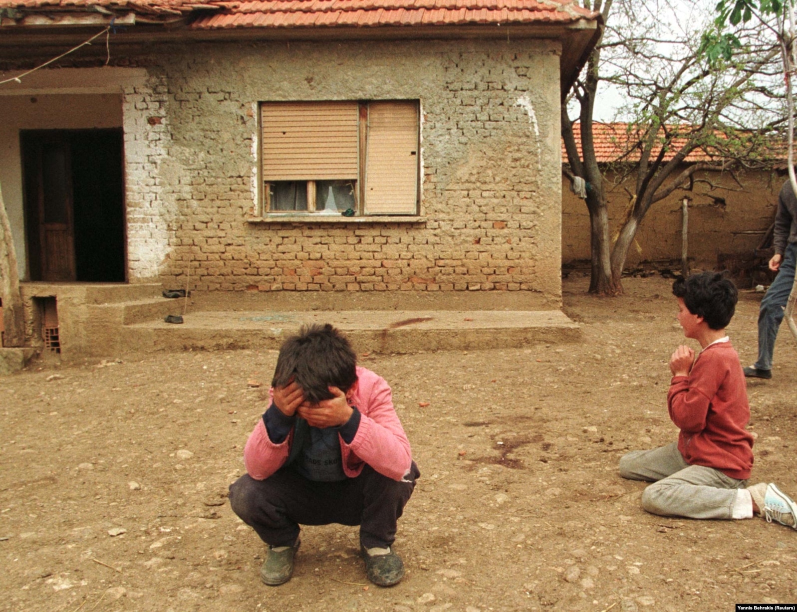 Fëmijët shqiptarë duke qarë jashtë shtëpisë ku u vranë dy prindër të rinj, së bashku me një grua tjetër, kur një mortajë serbe ra në oborrin e shtëpisë së tyre në Kosovë, më 3 maj 1998.