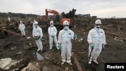 Japanese police officers in protective suits observe a moment of silence for those who were killed by the March 11 earthquake and tsunami as they search for bodies at a destroyed area in Minamisoma, Fukushima prefecture, in April 2011.