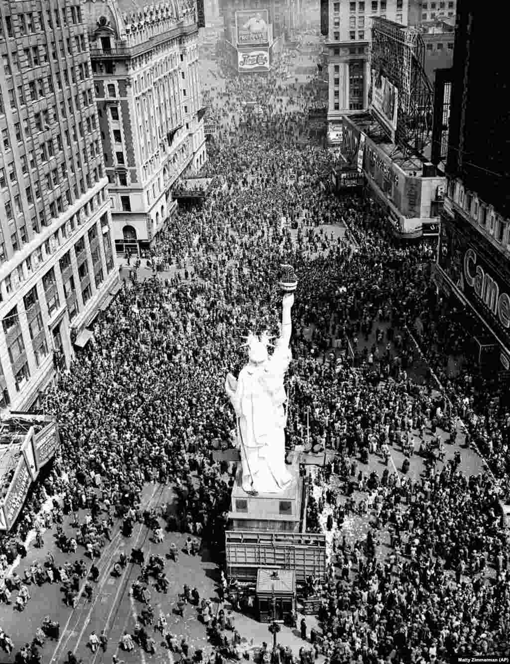 Crowds gather under a replica of the Statue of Liberty on Times Square. A reporter described the giddy scene: &ldquo;Here and there, a tipsy civilian &ndash; sometimes a serviceman &ndash; offered drinks to strangers. The drinks were eagerly accepted, mostly by teenagers.&rdquo;