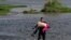 Menedékkérő venezuelai migráns, karjában egy idős nővel a Texast Mexikótól elválasztó Rio Grande folyón, 2021. május 26-án