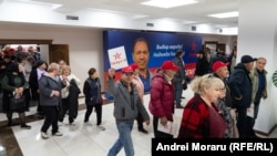Oameni, pe holul Casei de Cultură din Comrat unde s-a lansat în campania pentru funcția de bașcan Fiodor Gagauz. Pe fundal, un panou electoral cu acesta.