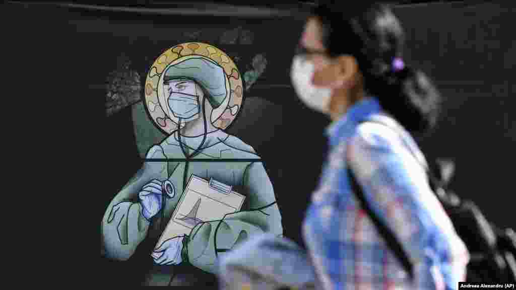 A woman walks by a depiction of medical staff wearing protective equipment, executed in the style of an Orthodox icon in Bucharest, Romania, on April 29.