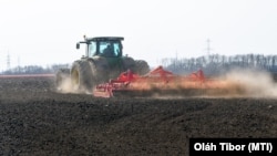 Szántóföldet boronál egy traktor.