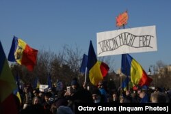 „Vakcin macht frei” de pe pancarta manifestanților anti-restricții din Piața Victoriei parafrazează mesajul macabru care îi întâmpina pe victimele Holocaustului la Auschwitz „Arbeit macht frei”/ „Munca vă va face liberi”. Ca detaliu semnificativ, deținuții evrei care au fost obligați să facă poarta de fier forjat erau artiști și arhitecți Bauhaus, stil marcat în întreaga Europă de artiști evrei, foarte apreciat și astăzi. Victimele l-au folosit ca un subtil gest de rezistență contra călăilor lor.