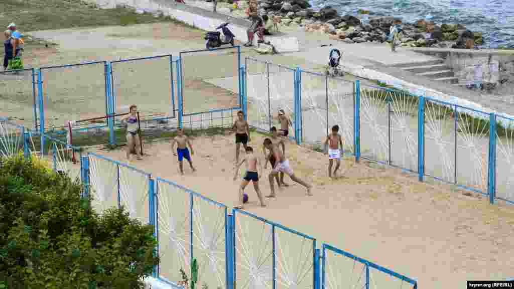 На спортплощадке у входа на пляж мальчишки играют в футбол