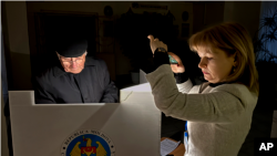 Un funcționar electoral ajută un alegător cu lanterna telefonului în timpul unei pene de curent în Chișinău, 20 octombrie 2024.