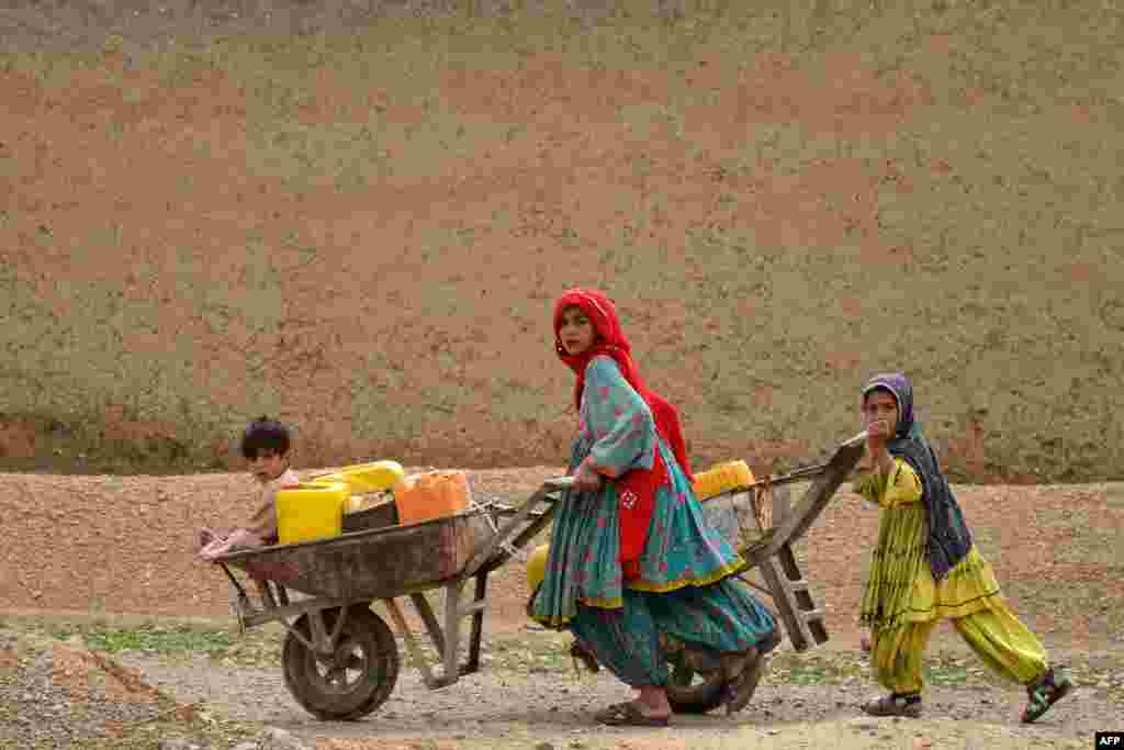 Afghan Kochi nomad girls push wheelbarrows as they fetch water along a street in the Daman district of Kandahar Province. 