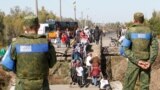 Localnici traversând un pod care a fost distrus în timpul luptelor, sub supravegherea militarilor. Stația Luhansk, 25 septembrie 2019