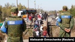 Localnici traversând un pod care a fost distrus în timpul luptelor, sub supravegherea militarilor. Stația Luhansk, 25 septembrie 2019