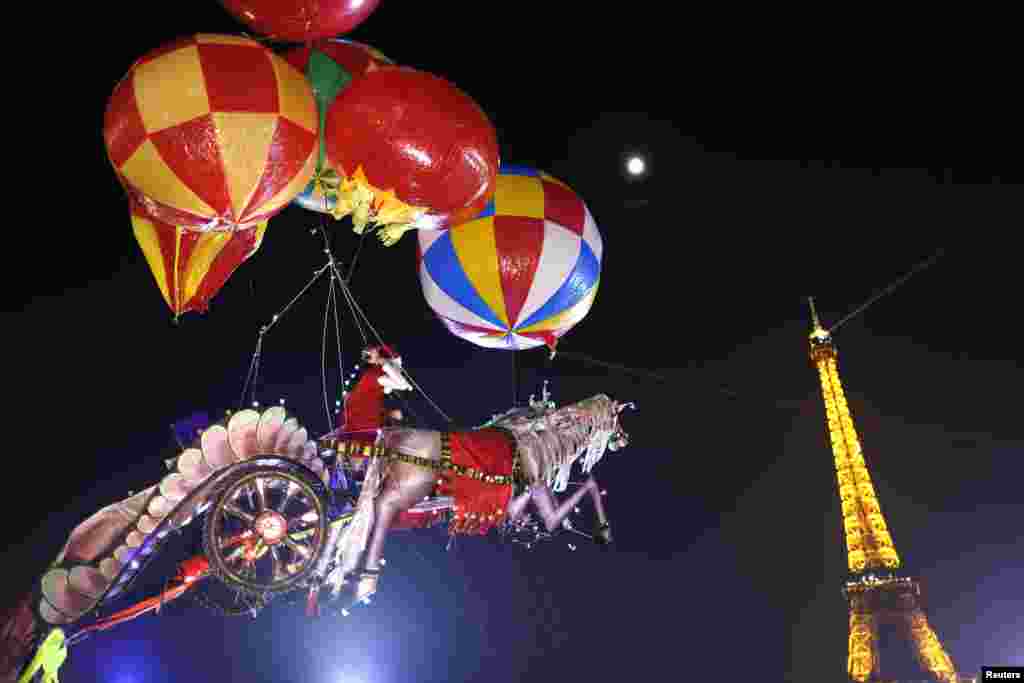 Helium-filled balloons suspend a Santa Claus figure riding a horse-drawn chariot made of balsa wood, created by artist Nasser Volant, near the Eiffel Tower in Paris. (Reuters/Charles Platiau)