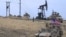 U.S. military vehicles drive past an oil pump jack on the countryside of Syria's northeastern city of Qamishli, November 1, 2019