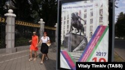 Сайлау туралы жарнаманың қасынан өтіп бара жатқан адамдар. Краснодар, Ресей. (Көрнекі сурет.)