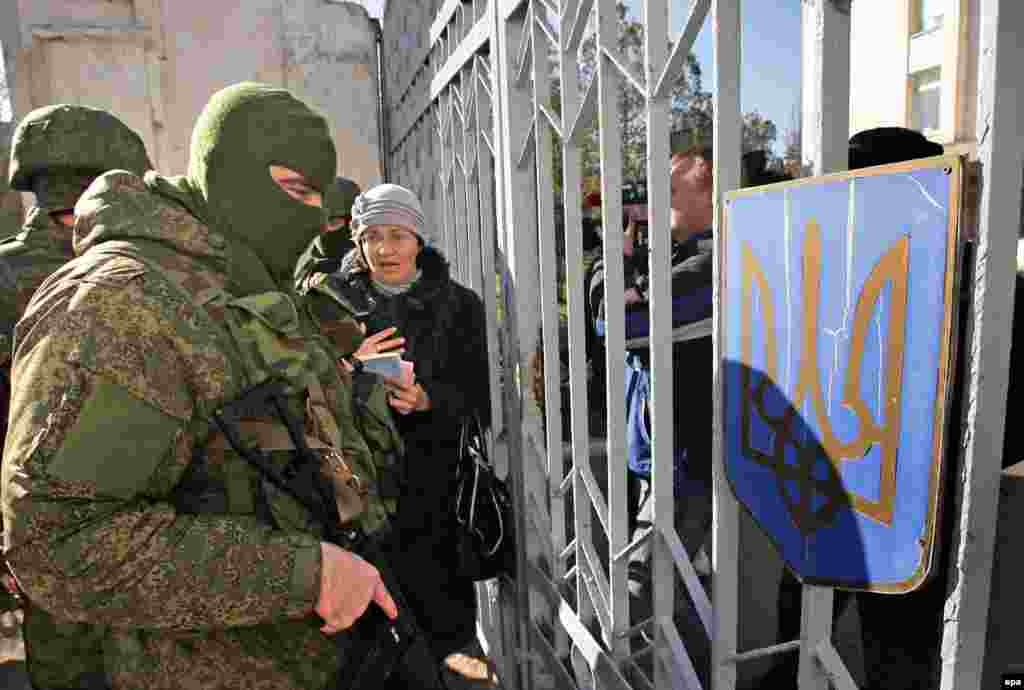 Украинская женщина обращается к военному в маске у входа на военно-морскую базу в Феодосии. 