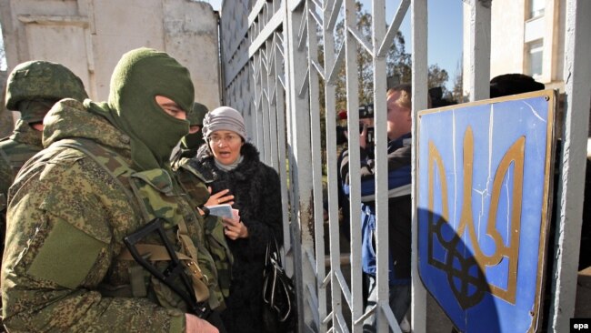 Украинские женщины разговаривают с мужчинами, одетыми в российскую военную форму, которые блокируют украинских военных в Новоозерном недалеко от Евпатории, 3 марта 2014 года
