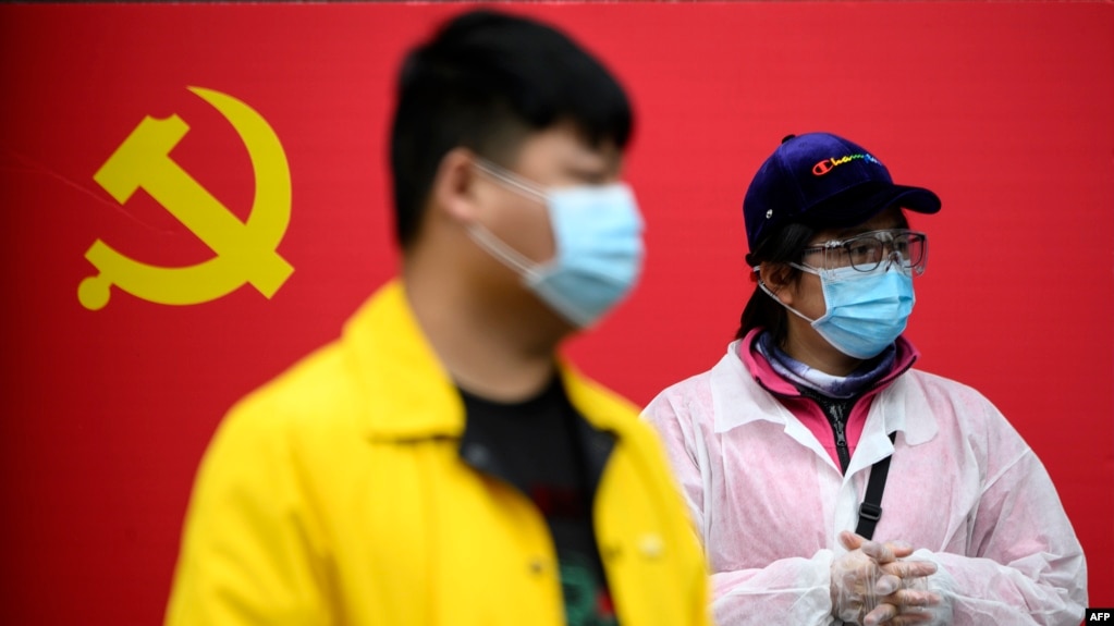 دو نفر که ماسک به صورت زده‌اند در مقابل حزب کمونیست چین در شهر ووهان، مرکز شیوع کرونا، ایستاده‌اند.
