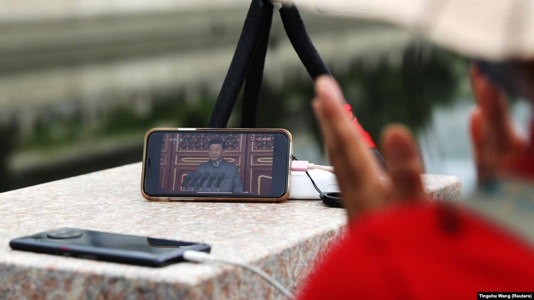 Žena aplaudira dok sluša govor kineskog predsjednika koji prati na mobilnom telefonu, Peking, 1. jul 2021.