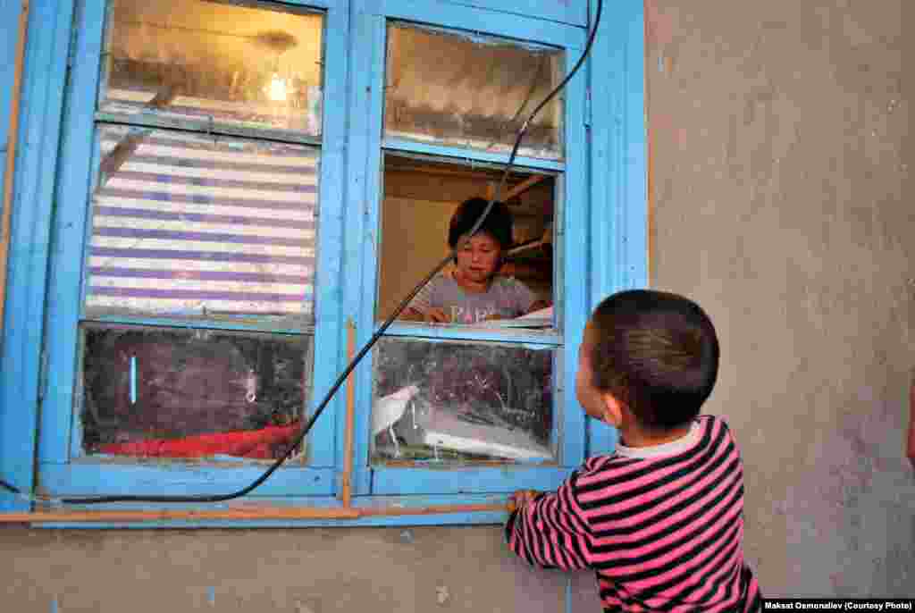 Младший брат наблюдает через окно за сестрой Айбике, которая учит уроки.&nbsp; Село Ачы, Сузакский район Джалал-Абадской области.