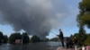Pescari pe malul unui râu, în timp ce fumul se ridică de la depozitele Wildberries din Koledino, regiunea Moscovei, după un atac cu drone ucrainene, 16 august 2026
