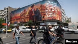 People pass a billboard depicting Iran's late Supreme Leader Ayatollah Ali Khamenei embracing late senior Iranian military commander General Qassem Soleimani, in Tehran on June 28. 