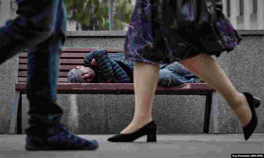 Люди проходят мимо человека, спящего на скамейке на одной из улиц Москвы, Россия