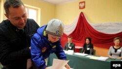 A man with his child casts his vote at a polling station during parliamentary elections in Przecieszyn, south Poland on October 25. 