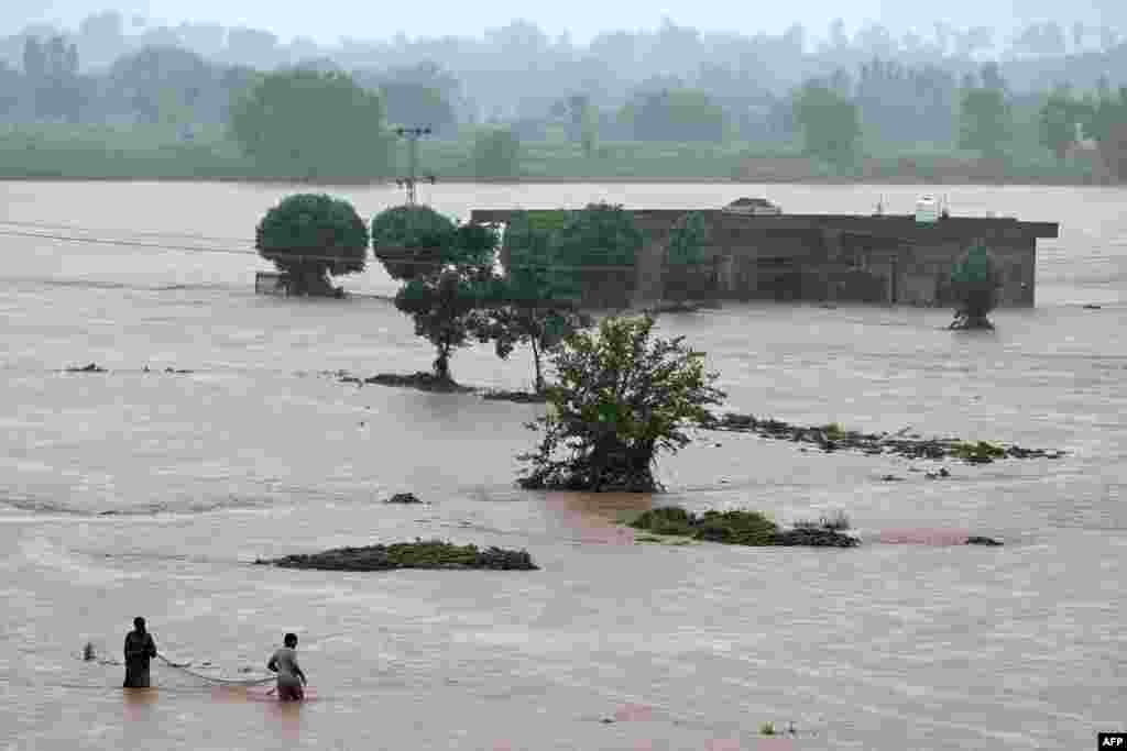 Local people catch fish in floodwaters near a partially submerged house during heavy monsoon rains in the village of Ladian in Pakistan's Punjab Province.