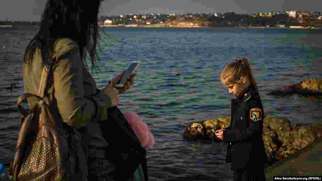 Женщина фотографирует дочь на набережной. Надпись на нашивке у школьницы: &laquo;Юный патриот&raquo;