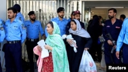 Žena sa bebom prolazi pored policajaca dok napušta odjeljenje nakon smrtonosnog požara u bolnici Pakistanskog instituta medicinskih nauka u Islamabadu, Pakistan, 26. augusta 2026.