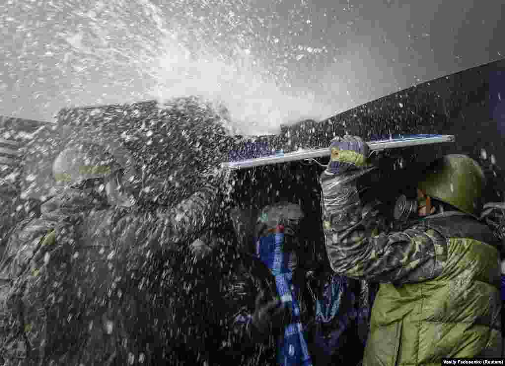 Protesters take cover from water sprayed from a fire engine.