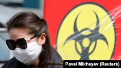 Коронавирус қаупі туралы баннердің жанында тұрған маска таққан қыз. Алматы, 24 наурыз 2020 жыл.