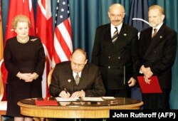 Ministrul de Externe ceh, Jan Kavan (așezat), semnează documentul de aderare la NATO a Cehiei. În stânga, secretarul de stat SUA, Madeleine Albright, în dreapta: miniștrii de externe din Ungaria (Janos Martonyi) și Polonia (Bronislaw Geremek). 12 martie 1999, Independence, MO.