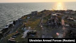 Ukrán katonák sétálnak el a lerombolt épületek mellett a Kígyó-szigeten az ukrajnai Odessza régióban 2022. július 7-én