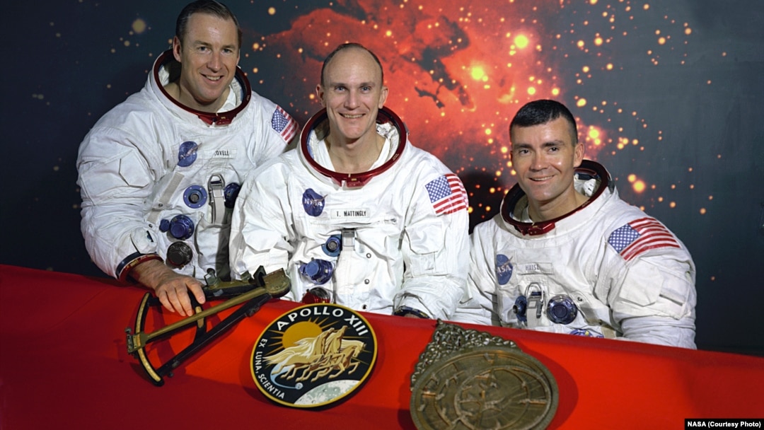 Echipajul inițial Apollo 13, James A. Lovell - Thomas K. Mattingly - Fred W. Haise, cu însemnele Apollo 13 și un model de sextant și un astrolab, instrumente străvechi de navigație. Mattingly a fost expus rujeolei și a fost înlocuit cu John L. "Jack" Swigert Jr.