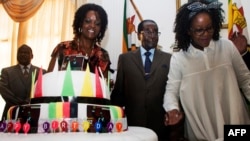 Президент Роберт Мугабе в окружении супруги Грейс Мугабе (слева) и дочери Боны (справа) стоит возле торта с именем клана Гушунго, к которому принадлежит Мугабе. Хараре, 22 февраля 2016 года.