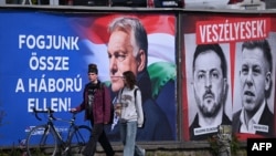 Dvoje mladih prolazi pored bilborda na kojem je prikazana fotografija mađarskog premijera uz poruku "Ujedinite se protiv rata", dok su portreti ukrajinskog predsjednika Volodymyra Zelenskog i opozicionog lidera Petera Magyara praćeni natpisom "Oni su opasni".