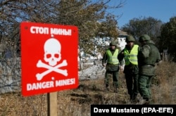 Pro-Russian militants stand next to a sign saying "Danger mines!" as OSCE observers inspect the situation from their side close to the front line in the village of Petrovske, in the Donetsk region, on October 10.