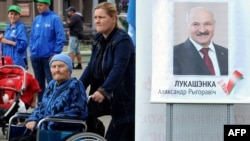 Belarus -- People walk past a poster bearing the image of Belarusian President Alyaksandr Lukashenka as his supporters collect signatures to register him as a candidate for the October 11 presidential elections, in Minsk, September 19, 2015