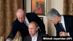 Prigojin (stânga) și premierul rus de atunci, Vladimir Putin (centru), în timpul unui dineu cu cercetători și jurnaliști străini în afara Moscovei, în noiembrie 2011.