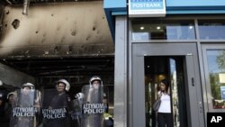 A woman leaves a bank as riot police guard the entrance of the Greek Finance Ministry during a protest by garbage collectors in Athens on September 27.