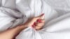 Hand sign orgasm of a woman on a white bed, Hand of female pulling white sheets in ecstasy, feeling and emotion concept